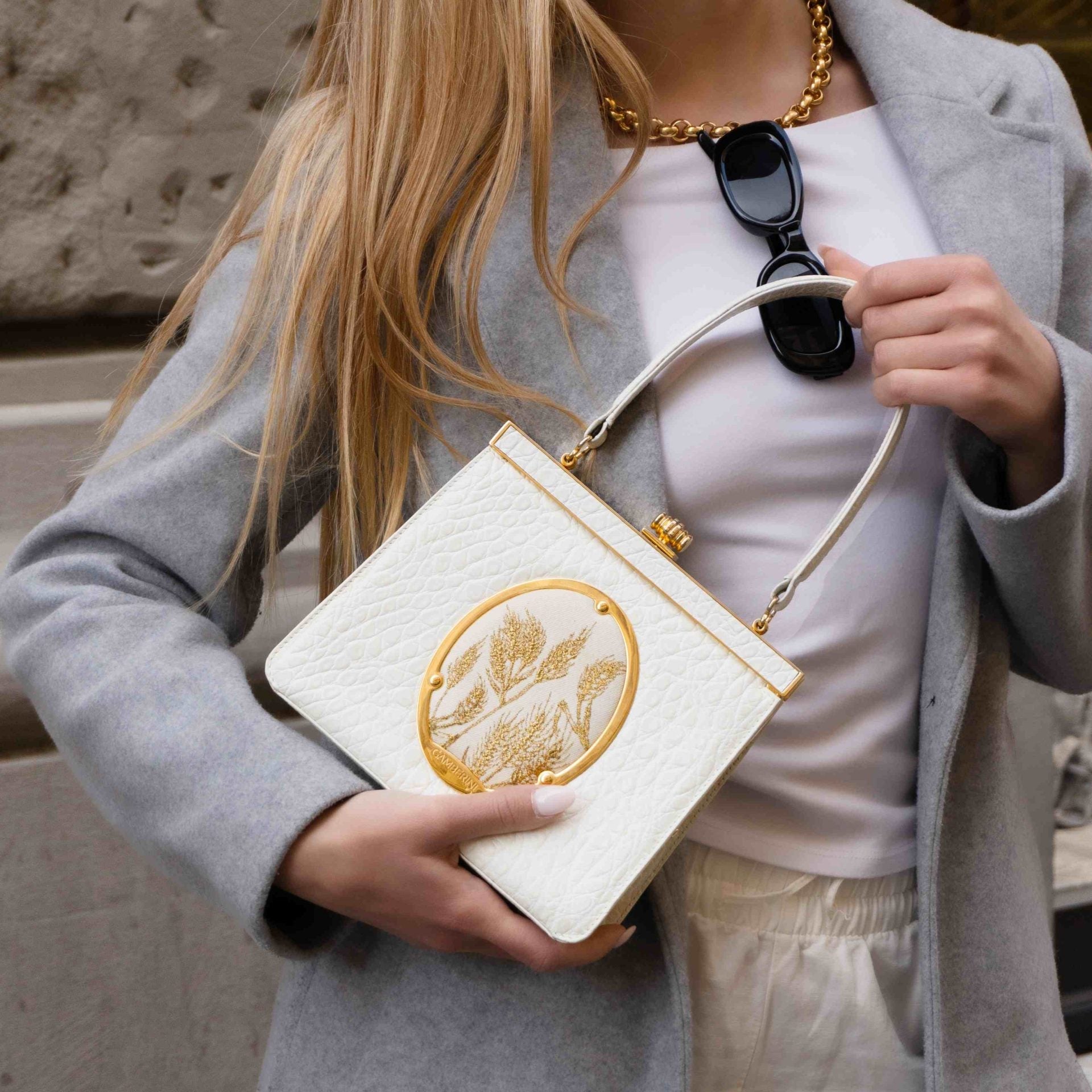 Woman holding a white clutch with gold design outdoors